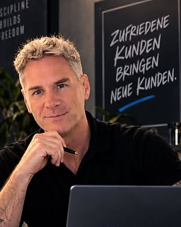 Sascha Emmerich am Schreibtisch, hinter ihm eine Tafel: Zufriedene Kunden bringen neue Kunden.